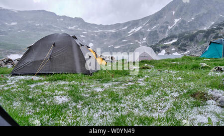 Zelte bei Hagel und Regen im Sommer, mittags am See, bucura Retezat Gebirge. Blick aus einem Zelt, mit vielen Hagelkörner in der Grünen gra Stockfoto