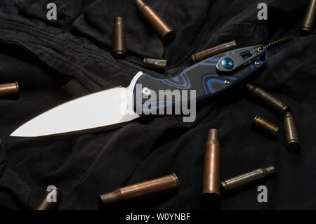 Taschenmesser auf schwarzem Stoff. Zerstreut Hülse. Messer und Patrone Fall auf Schwarz. Stockfoto