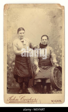 Original Sepia getönte viktorianische CDV (Carte de Visite) Porträt von Grubenbrauen Mädchen (Broo Lasses oder wenches) tragen Clogs und Hosen unter ihren Schürzen, posiert mit den Werkzeugen ihres Fachs - eine Schaufel und Sieb. Sie arbeiteten an der Grubenbank (oder Braue) an der Oberseite des Schachts und pflückten Steine aus der Kohle, auf dem Kohlefeld, fotografiert von John Cooper's Studio, Wigan, Greater Manchester, Lancashire, U.K. um 1870 Stockfoto