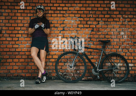 Frau, die neben ihrem Fahrrad posiert vor dem Hintergrund der Mauer. Stockfoto