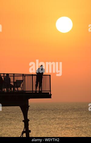 Aberystwyth, Wales, UK. 28. Juni 2019. UK Wetter: Menschen auf der Pier am Meer bei Sonnenuntergang in Aberystwyth an einem drückend Sommer Abend nach einem Tag der unversehrten blauen Himmel und warmen Sonnenschein. Das Land ist in Richtung der heißeste Tag des Jahres so weit wie eine Feder der glühend heiße Luft driftet in vom Kontinent. Foto Keith Morris/Alamy leben Nachrichten Stockfoto