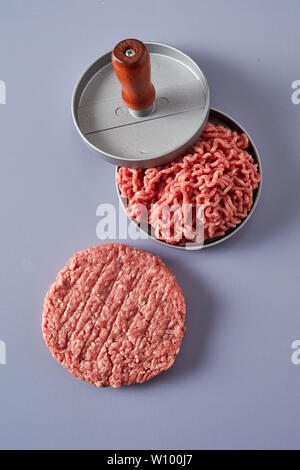 Frischem Boden oder Hackfleisch/Faschiertes rohes Rindfleisch in einer patty Teekocher komprimierte während der Vorbereitung hausgemachte Hamburger mit einem fertigen runde Patty neben Stockfoto