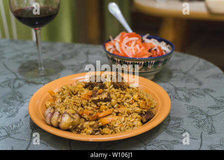 Pilav mit roten Wein in ein Glas und eine Salat von Tomaten und Zwiebeln. Orientalische Schale mit Reis und Fleisch auf dem östlichen Platte. Stockfoto
