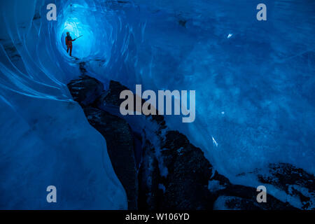 Ein tiefes, dunkles Eis Höhle mit einem Mann, der in der Rückseite. Er ist von der Sonne durch eine dünne Eis glänzenden beleuchtet. Stockfoto