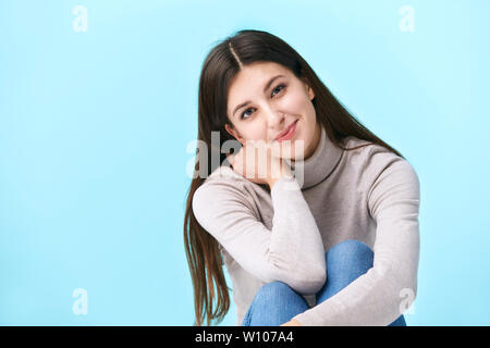 Studio Porträt einer wunderschönen kaukasische Frau, sitzen auf dem Boden, in die Kamera lächeln suchen, auf blauem Hintergrund isoliert Stockfoto