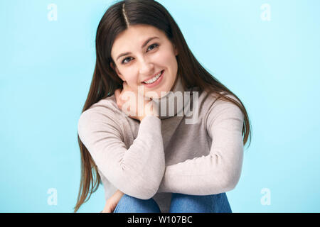 Studio Porträt einer wunderschönen kaukasische Frau, sitzen auf dem Boden, in die Kamera lächeln suchen, auf blauem Hintergrund isoliert Stockfoto