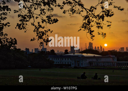 Menschen genießen den Sommeruntergang im Greenwich Park mit Blick auf das maritime Museum und das Stadtzentrum in London, England Stockfoto