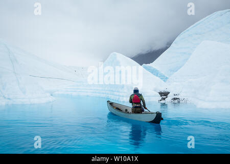 Mann Paddles eine volle Größe aufblasbares Kanu über einem tiefblauen Gletschersee durch Wasser der schmelzenden Matanuska Gletscher in Alaska geschnitzt. Stockfoto