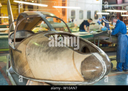 Menschen in blauen Roben bauen ein Flugzeug in der Fabrik. Arbeitnehmer in Overalls an den Einzelheiten des Flugzeugs. Stockfoto