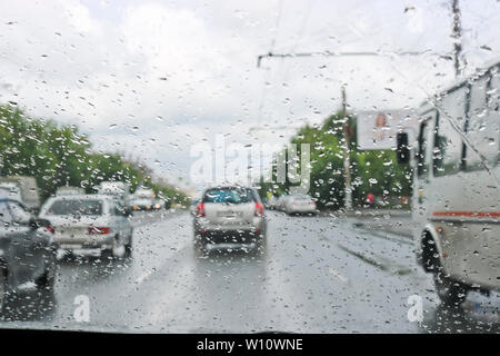 Regentropfen auf der Windschutzscheibe des Autos. Selektive konzentrieren. Der Blick aus dem Autofenster auf der Fahrbahn. Schlechte Sicht. Stockfoto