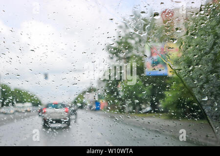 Regentropfen auf der Windschutzscheibe des Autos. Selektive konzentrieren. Der Blick aus dem Autofenster auf der Fahrbahn. Schlechte Sicht. Stockfoto