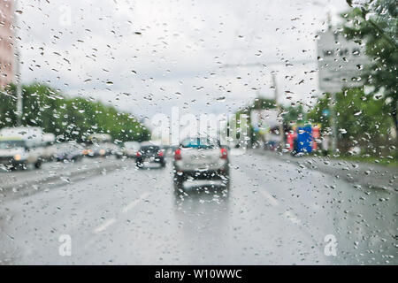 Regentropfen auf der Windschutzscheibe des Autos. Selektive konzentrieren. Der Blick aus dem Autofenster auf der Fahrbahn. Schlechte Sicht. Stockfoto