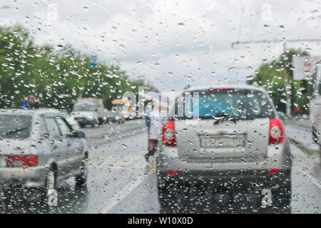 Regentropfen auf der Windschutzscheibe des Autos. Selektive konzentrieren. Der Blick aus dem Autofenster auf der Fahrbahn. Schlechte Sicht. Stockfoto