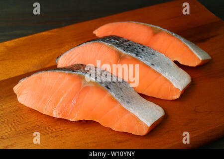 Drei Stücke geschnittenen frischen, rohen Lachs auf einer hölzernen Schneidebrett Stockfoto