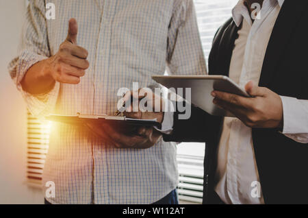 Zwei Partner Business Mann mit Daumen nach oben und Investor sprechen und lesen Informationen über Finanzstatistiken in mobilen Tablet stehen im Büro Stockfoto