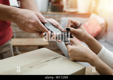 Frau Kunde anhängen Signatur in digitalen Mobiltelefon empfangen Parcel Post Box von Kurier mit Home Delivery Service Mann in der roten Uniform Stockfoto