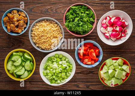 Zutaten für gesunde Ernährung in bunten Schalen auf einem Holztisch. Quinoa, rohem Gemüse und gebratenem Tofu Stockfoto