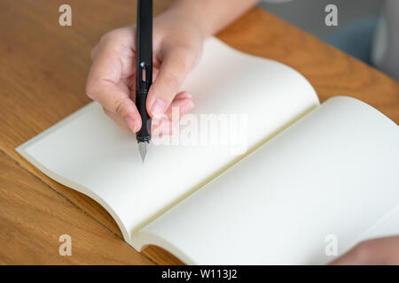 Asiatische Mädchen mit einem schwarzen Kugelschreiber in ein leeres Buch zu schreiben. Tagebuch schreiben Geschichten aufgezeichnet beeindruckend. Erinnerungen an einem hölzernen Tisch Stockfoto