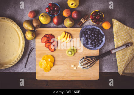 Vorbereitung von Obst Torte mit bunten Früchten und frischem Teig fertig zu Backen. Frische Lebensmittel Konzept. Stockfoto