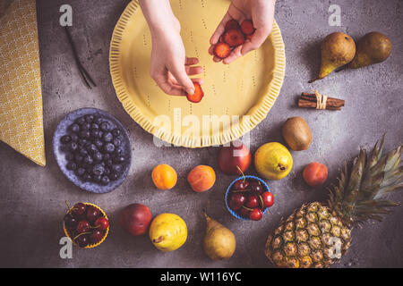 Weibliche Hände bereiten Obst Torte mit bunten Früchten und frischem Teig. Gesunde Ernährung Konzept. Stockfoto