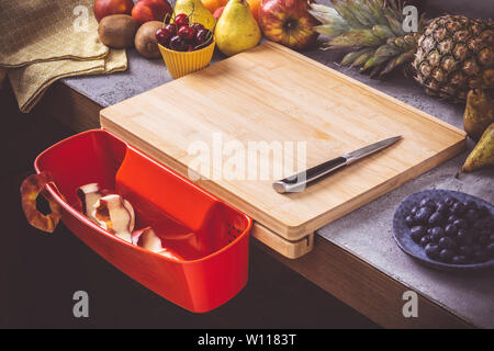 Schneidbrett mit roten Abfallbehälter mit frischen Früchten Hintergrund. Gesunde Ernährung vegane Rohkost Konzept. Stockfoto
