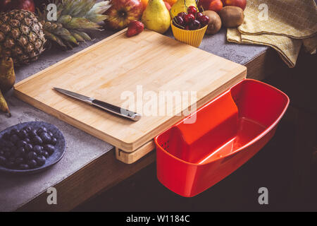 Schneidbrett mit roten Abfallbehälter mit frischen Früchten Hintergrund. Gesunde Ernährung vegane Rohkost Konzept. Stockfoto