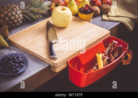 Schneidbrett mit roten Abfallbehälter mit frischen Früchten Hintergrund. Gesunde Ernährung vegane Rohkost Konzept. Stockfoto