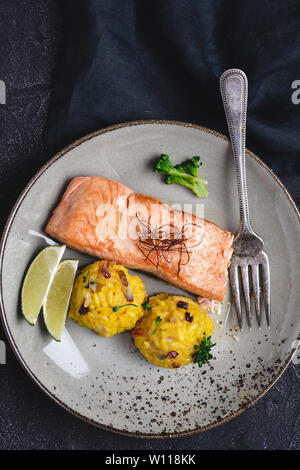 Gegrilltes Lachssteak mit gelben Risotto und Kalk auf Stein. Gesunde Ernährung Konzept. Stockfoto