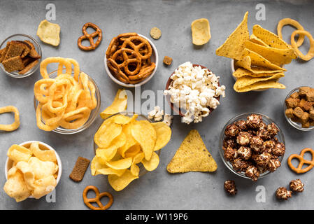 Sortiment von ungesunden Snacks: chips, Popcorn, nachos, Brezeln, Zwiebelringe in Schalen, Ansicht von oben, kopieren. Ungesunde Konzept essen. Stockfoto