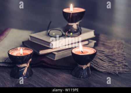 Brennende spa Aroma Kerzen in Kokosnussschalen, Plaid, Gläser und Bücher, gemütliche Home Interior Hintergrund Stockfoto