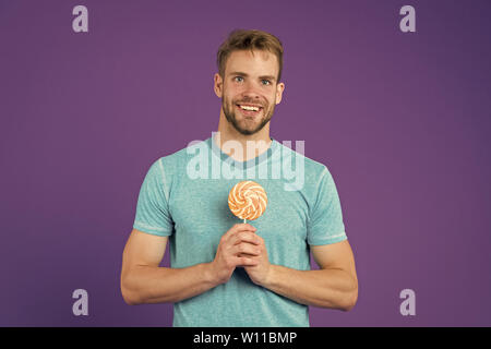 Zucker schädlich für die Gesundheit. Kerl halten Lollipop candy violett unterlegt. Mann schöner macho Essen großen bunten süßen Lutscher. Geschmack der Kindheit. Mann mit Borsten mag Lollipop. Cheat meal Konzept. Stockfoto