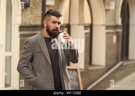 Kaffee trinken für Unterwegs. Geschäftsmann lumbersexual Erscheinungsbild genießen Sie Kaffee Pause aus Business Center. Entspannen und erholen Sie sich. Man bärtige hipster Pappbecher Kaffee trinken. Noch ein Schluck Kaffee. Stockfoto