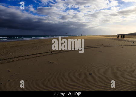 Schöne und windigen Strand bei Sonnenuntergang mit Menschen üben Kitesurfen in den Hintergrund und die Reifenspuren im Sand Stockfoto