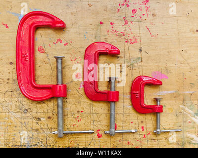 Drei rote Metall C Spannzangen auf Holz- Workbench Oberfläche Hintergrund. Stockfoto