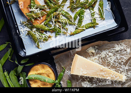 Ansicht von oben von Parmesan und Polenta panierte Snap Erbsen gebraten auf das Backblech. Zutaten auf einer konkreten Tabelle, Ansicht von oben, flatlay Stockfoto