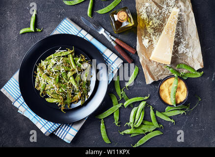 Ansicht von oben von knusprig gebratene Polenta und Parmesan paniert Snap Erbsen auf einem Teller serviert. Zutaten auf einer konkreten Tabelle, Ansicht von oben, horizontal Stockfoto