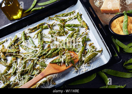 Ansicht von oben knusprig Parmesan und Polenta panierte Zuckerschoten gebraten auf das Backblech. Zutaten auf einer konkreten Tabelle, Ansicht von oben, flatlay, Clo Stockfoto