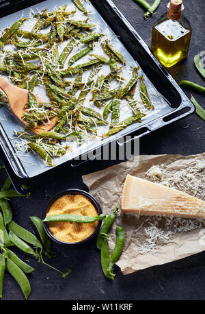 Parmesan und Polenta knusprig paniert Snap Erbsen gebraten auf das Backblech. Zutaten auf einer konkreten Tabelle, vertikale Ansicht von oben Stockfoto