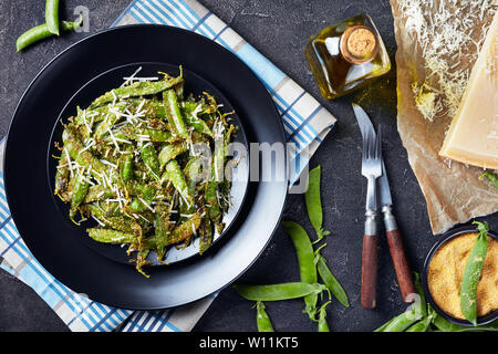 Knusprig gebratene Polenta und Parmesan paniert Snap Erbsen auf Teller serviert. Zutaten auf einer konkreten Tabelle, horizontale Ansicht von oben, flatlay, close-u Stockfoto