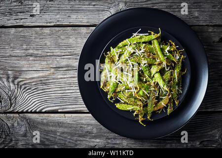 Ansicht von oben der knusprig gerösteten Parmesan und Polenta panierte Zuckerschoten Pommes frites serviert auf einer schwarzen Platte auf einem Holztisch, von oben betrachten, flatlay, emp Stockfoto