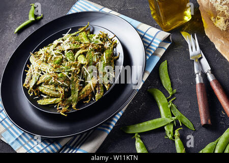 Knusprig gebratene Polenta und Parmesan paniert Snap Erbsen auf Teller serviert. Zutaten auf einer konkreten Tabelle, horizontale Ansicht von oben Stockfoto