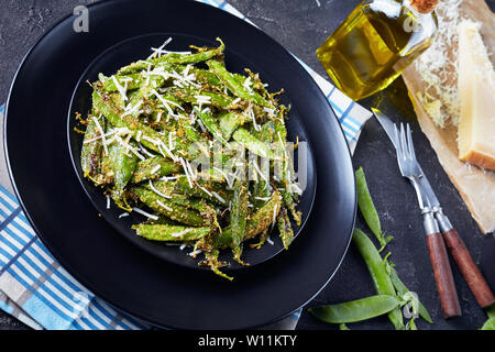 Knusprig gerösteten Parmesan und Polenta panierte Zuckerschoten Pommes auf Teller serviert. Zutaten auf einer konkreten Tabelle, horizontale Ansicht von oben, close-up Stockfoto