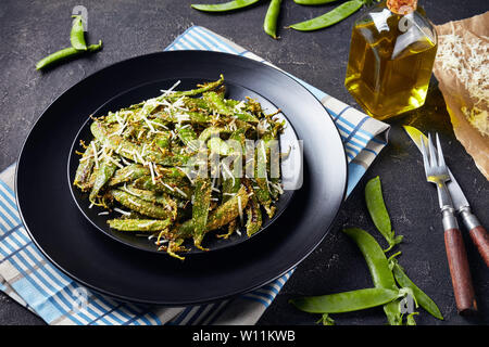 Knusprig gebratene Polenta und Parmesan paniert Snap Erbsen auf Teller serviert. Zutaten auf einer konkreten Tabelle, horizontale Ansicht von oben Stockfoto