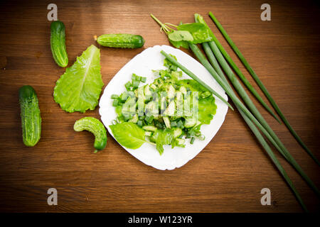 Frischer Salat mit Gurken und Grüns in einen Teller auf einem Holztisch Stockfoto