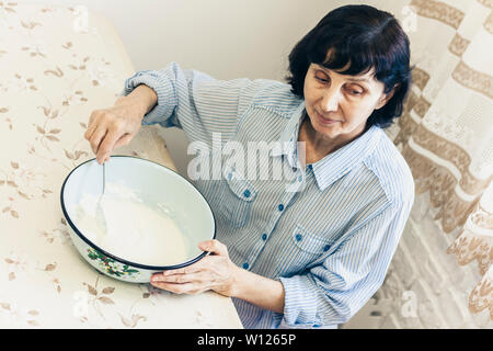 Im mittleren Alter brünette Frau kneten Sie den Teig für die Knödel in blaue Schale Stockfoto