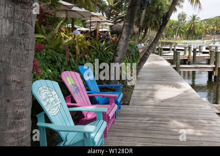 Adirondack Stühlen sitzen auf der Promenade unter Palmen außerhalb Guanabanas Restaurant entlang der Uferpromenade am Jupiter Inlet in Florida, USA. Stockfoto