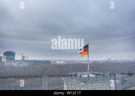 Verschwommen deutscher Flagge und städtischen Skyline durch ein Fenster voller Regentropfen an einem regnerischen und bewölkten Tag gesehen. Auf der Vorderseite konzentriert, Fenster. Kopieren Sie Platz. Stockfoto