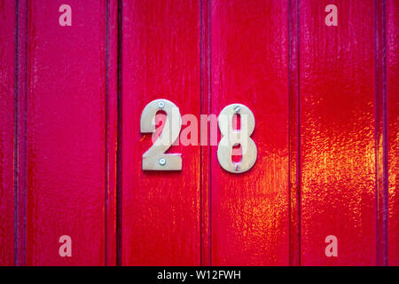 Haus Nummer 28 auf eine helle rote hölzerne Eingangstür aus Planken Stockfoto