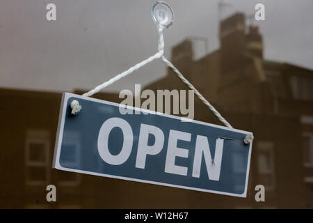 Open Schild hängt schief hinter einem Schaufenster mit Häusern im Glas reflektiert Stockfoto