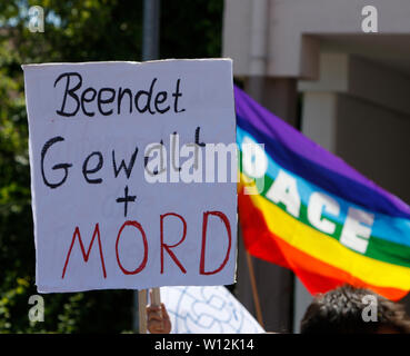 Ramstein, Deutschland. 29. Juni 2019. Eine Demonstrantin hält ein Schild mit der Aufschrift "Gewalt und Mord". Ein Regenbogen Frieden Flagge Fleece. ein paar tausend Friedensaktivisten aus dem Stopp der Air Base Ramstein Kampagne außerhalb der US-Airbase Ramstein protestiert. Der Protest war das Ende der diesjährigen Aktionswoche gegen die Airbase. Im Mittelpunkt der Veranstaltungen in diesem Jahr war die angebliche Beteiligung der Airbase in die drone Kriegsführung der US Air Force im Nahen Osten und in Afrika und Anruf Ramstein nicht für einen künftigen Krieg mit dem Iran. Stockfoto